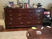 Front view of wooden dresser with 9 drawers and ornate metal handles, showing its dark wood finish and decor items on top