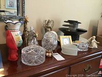 Overall lot showing various figurines including angels and giraffes, glass trinket boxes, vases, and electric tiered fountain on dresser