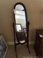 Front view of the wooden freestanding oval mirror, showing the full mirror surface and wooden frame with turned side posts.