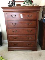 Front view of the wood chest of drawers showing five drawers with brass handles and overall condition.
