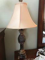 Single pineapple design table lamp with beige shade shown against a wall near furniture, close-up view of ornate base and shade.