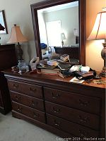 Front view of the wooden dresser with attached mirror showing six drawers and items on top, including lamps not included in sale.
