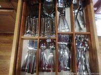 Full open drawer showing organized silver-toned knives, forks, spoons, and serving spoons laid in a wooden flatware organizer.