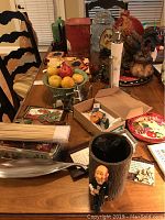 Photo showing variety of rooster-themed kitchen decor items on a wooden table including plates, bowls, figurines, and kitchenware.