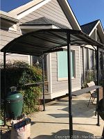 Side view of black metal handmade pergola set on patio with curved roof and vertical posts. No grills included.