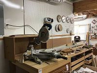 Makita mitre saw bolted to a wooden workbench with scattered wood pieces and tools.