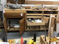 Woodworking cabinets and drawers holding various tools and wood pieces, with some drawers open showing contents.