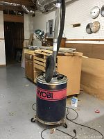 Full view of a Ryobi wood shop vacuum in a workshop with visible attached hose and wheels.
