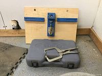 Photo showing the Kreg branded gray drill bit case with a silver metal locking plier vise resting on top.