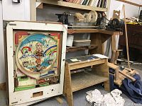 Wide view of vintage Pachinko game cabinet next to wooden work bench with GE grinder motor attached.