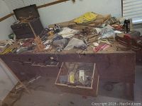 Overall photo of workbench crowded with various woodworking tools, materials, and vise on right side.