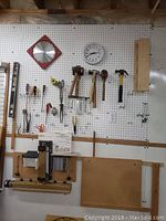 View of pegboard with assorted hand tools including hammers, screwdrivers, scissors, snips, saw blade, levels and clock.