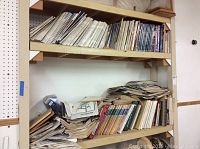 Wide shelf view showing shelves filled with stacked books and manuals in varied sizes and conditions, some stored upright and others stacked horizontally