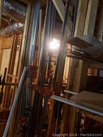 Multiple long F-style metal bar clamps with orange trigger handles leaning against wall framing