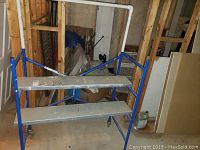Blue metal scaffold with two shelves, caster wheels, basement surroundings