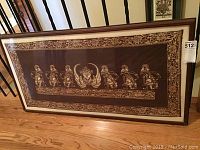Framed long rectangular batik art panel resting on floor, showing full piece with brown wooden frame and cream matting.