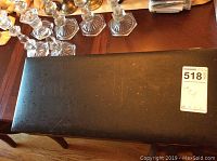 Closed black rectangular case with metal clasps showing wear marks on a wood surface with crystal candle holders nearby.