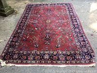 Full view of rug laid flat on concrete showing red field and navy floral border