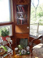 Full view of wooden bookshelf cabinet with 3 tiers of shelves filled with books, drop front desk, and single drawer below with turned legs.