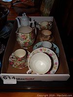 View of assorted china items in box including tea pot, cream, sugar, cups and saucers with floral designs.
