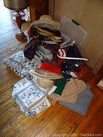 Sweaters, scarves, and fur and straw hats arranged on wooden floor with clear plastic storage boxes in background