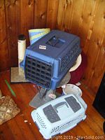 View of blue plastic cat taxi on scratching post with burgundy cat bed and a pet bowl visible behind, base of a small scratching post nearby