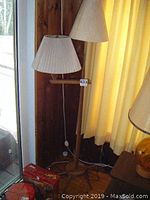 Photo of vintage wooden floor lamp showing full height and fabric shade positioned beside yellow curtains and wooden wall.