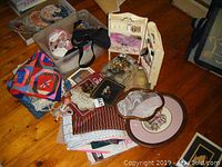Overall lot with fabrics, thread box, buttons, books, doll, and other sewing accessories spread on wooden floor.