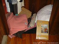 Photo showing folded wool blankets in various colors and a white feather duvet in the corner of a wooden room.