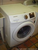 Photo of white Samsung front load washer showing overall appliance with visible front door and top panel.
