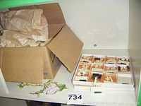 Box containing a compartmentalized tray with multiple ceramic table markers and some paper packing.