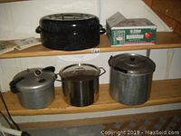 Shelf with large black enamel roaster, partial box of Bernardin canning sealers, and two large metallic canning pots.