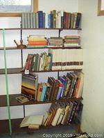 Five shelves filled with vintage hardcover books of varying sizes and colors. Books include travel, history, novels, and encyclopedias. Two books appear signed inside.