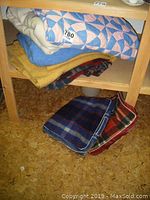 Side view of stacked blankets and quilt on wooden shelf showing different colors and patterns.