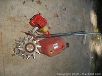 Red Echo Mantis gas tiller laying on concrete floor, visible red engine housing and metal blades, showing wear and usage.