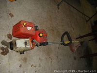 Fan angled view of the full Stihl FS 36 gas trimmer next to two red fuel cans on a concrete surface.