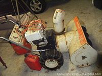 SnowBlower side view showing 33 inch snow intake, electric starter, pull start, and chained tires with fuel containers beside it.