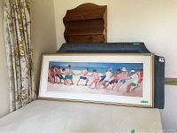 Front view of framed painting with beach tug-of-war scene leaning against furniture