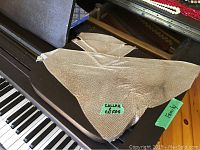 Silver mesh scarf-like collar laid over a piano surface, showing texture and shape, including metal snap closure.