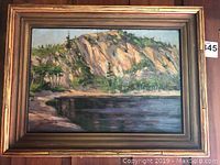 Front view of painting in gold frame hanging on wood-paneled wall