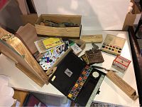 Top-down view of the art supplies spread on a table including paint palettes, brushes, paint tubes, pencils, and accessories.