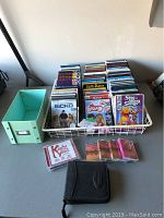 Front view of DVDs in metal rack, green box beside rack, music CDs and black DVD case on table