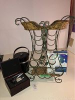 Photo of green metal wine storage rack with woven basket holders, black ice bucket, wooden box with corkscrew, and boxed wine glass arranged together