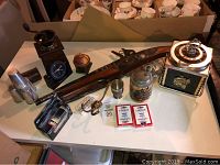 Overview of all items showing ornamental gun, coffee grinder, ice bucket, playing cards, metal cup, stein, and other metal kitchen and decor pieces arranged on table.
