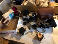 Full view of lot showing vintage SLR camera with lenses, camera cases, flash unit, tape eraser and accessories arranged on table