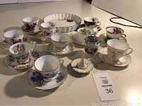 Wide view of set of teacups, saucers and quiche plate on a table, showing different patterns and gold rims.