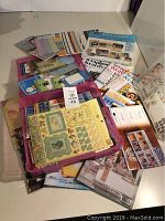 Photo of a collection of scrapbooking magazines, paper embellishments in plastic containers, and various crafting tapes and tools spread on a table.