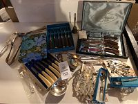Photo showing all knife sets, serving utensils, and handbell on display table.