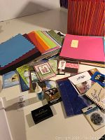 Overview photo showing colored paper sheets, handmade greeting cards, glue, and crafting accessories spread on a table.