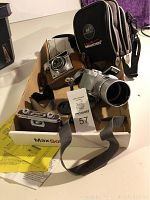 Boxed lot of two vintage cameras with straps, lens caps, lens hood, and Monster brand binoculars case.